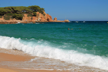  The running sea wave on the sandy beach against the background of the rock.