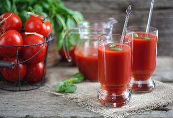 Tomato juice in glasses and tomato on wooden table on wooden background