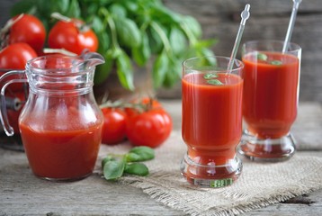 Tomato juice in glasses and tomato on wooden table on wooden background