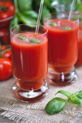 Tomato juice in glasses and tomato on wooden table on wooden background