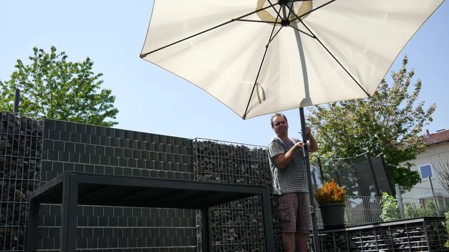 A man opens an umbrella from the sun on the terrace