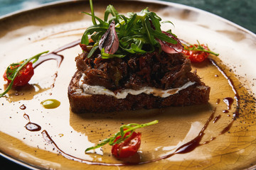 Bread with stewed meat baked onions and arugula on plate, close-up. Luxury delicious food. 