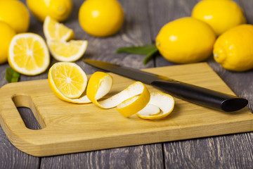 Whole lemons and pieces of fruit with peel on wooden Board next to knife