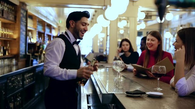 Smiling bartender pouring beverages and talking to cheerful visitors in bar