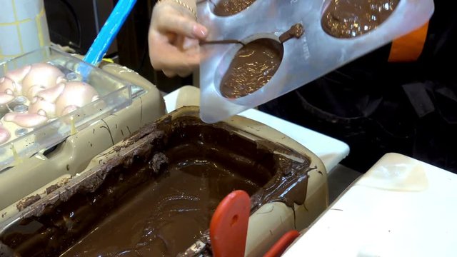 Chocolate making. Professional confectioner woman pours warm melted chocolate in plastic molds. HD video