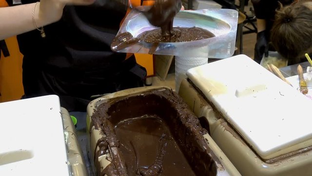 Chocolate egg making. Professional confectioner woman pours warm melted chocolate in plastic molds. HD video