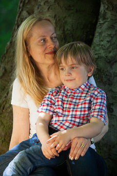 Mother and son (5-6) sitting on his mother at the foot of a large tree trunk