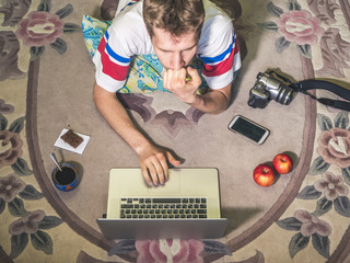 young man at home lying on the carpet and workingwith a laptop