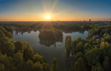 Die Sonne geht unter über dem Englischen Garten von München, ein Luftbild mit einer DJI Mavic Drohne aufgenommen zum Sonnenuntergang über dem Kleinhesseloher See mit Tretbooten im Vordergrund