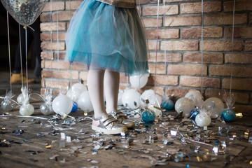 Birthday of the child. A baby girl in silvery sneakers and a sumptuous tulle skirt. On the floor are small balloons