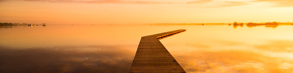 beautiful sunrise on a lake with a wooden dock | panorama