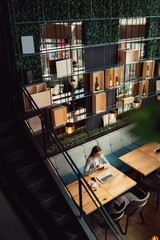 Young woman at a cafe, working on a laptop. Bird's eye perspective.