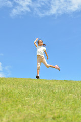 Fototapeta na wymiar 芝生広場でジャンプする女の子（青空）