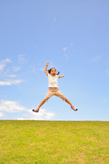 Fototapeta na wymiar 芝生広場でジャンプする女の子（青空）