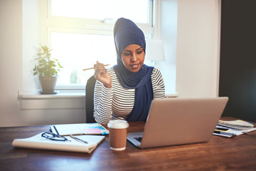 Smiling Arabic female entrepreneur working on a laptop at home
