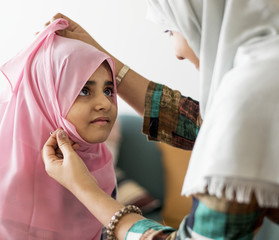 Muslim mother putting on a hijab on her little daughter