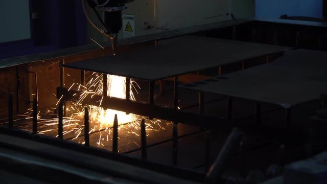 Close-up of the CNC laser cutting machine cutting the metal plate with the sparking light. Modern sheet metal manufacturing process.