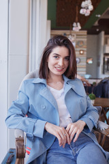 Young model look woman with long brown hair is sitting in a coffee shop during the brunch. Caucasian female with red lipstick on the lips is looking down while sitting at the table in the cafe.