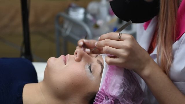 Permanent makeup. Eyelash Extension Procedure. Woman Eye with Long Eyelashes. Professional stylist lengthening female lashes. Eyelash extension procedure - master and a client in a beauty salon