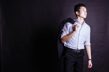 handsome Hispanic elegant man in black suit on grey background, holding the coat over his shoulder. Handsome young man with white shirt and tie carrying his jacket over shoulder isolated over white.