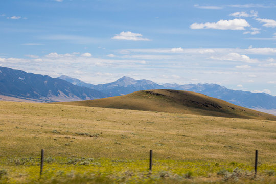 Rolling hills, mountains, and cloudy blue sky in summer. Montana, USA.