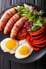 Fried sausages wrapped in bacon, eggs and fresh salad close-up. Vertical top view