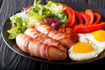 Breakfast Pigs in blankets fried sausages wrapped in bacon, eggs, sauce and fresh salad close-up. horizontal