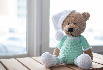 Brown stuffed animal teddy bear in mint-colored clothes and white hat on the wood.