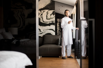 Contemporary businessman in white casual standing in the middle of hotel room with baggage