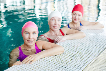 Fototapeta premium Group of mature women in swimwear sitting in swimming-pool and looking at you