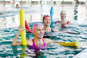 Smiling mature female in swimwear and two more active women listening to trainer advice during...