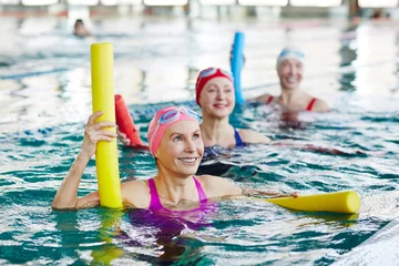 Fotobehang Gymnastiek Smiling mature female in swimwear and two more active women listening to trainer advice during gymnastics in water  © pressmaster