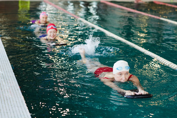 Row of mature women swimming in pool one after another while training at leisure center