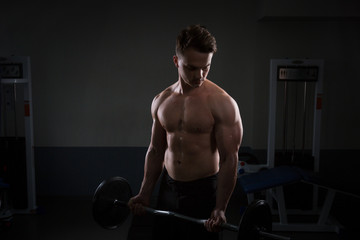 Close up of young muscular man lifting weights over dark background