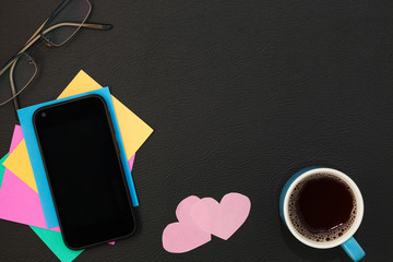 Smartphone with paper note and coffee cup on black leather background.