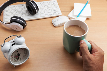 Hand holding coffee cup with business objects on wooden table.