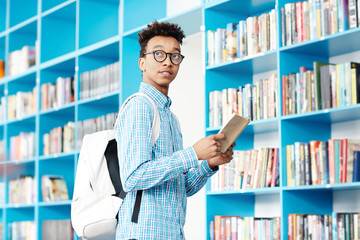 African-american student with book and backpack looking at library clock in order not to be late for next class