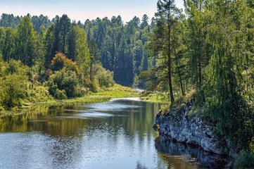 Warm summer river flows in the middle of rocks and green forest