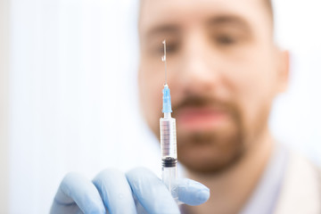 Gloved hand of doctor holding syringe with liquid medicine before making injection to sick patient