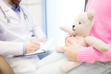 White teddybear in hands of little patient waiting for her doctor making prescriptions