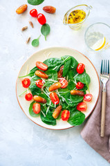 Fresh salad with spinach tomatoes cherry and dates served on a plate. White stone background. Healthy eating concept.