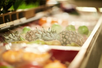 Fresh pineapple among other fruits in boxes or shelves of modern supermarket