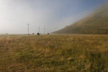 Fototapeta na wymiar View of Castelluccio di Norcia (Umbria, Italy) upland at morning, with power lines and mist