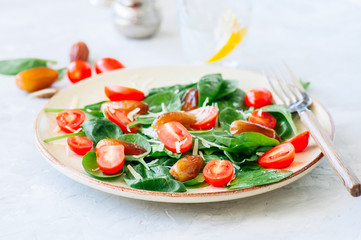 Fresh salad with spinach tomatoes cherry and dates served on a plate. White stone background. Healthy eating concept.