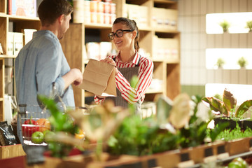 Happy shop assistant giving paper pack to man who chose something in supermarket