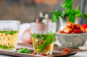 Traditional moroccan mint tea with dates on a vintage tray. White stone background.