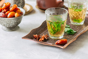 Traditional moroccan mint tea with dates on a vintage tray. White stone background.