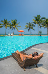 Woman at the swimming pool at the tropical resort with heaphones