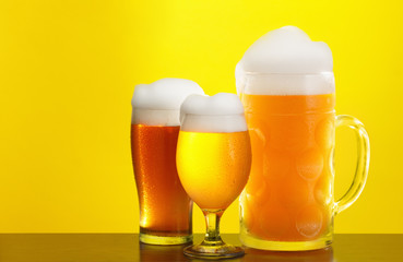 Mug and glass of beer close-up with froth over yellow background
