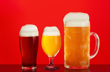 Mug and glass of beer close-up with froth over red background